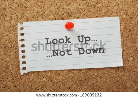 The phrase Look Up, Not Down typed on a paper note and pinned to a cork notice board.