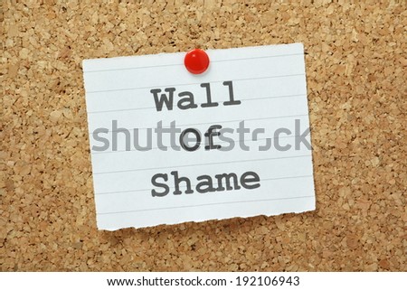 The phrase Wall of Shame typed on a piece of paper and pinned to a cork notice board