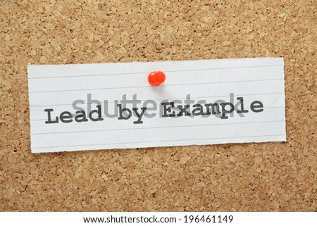 The phrase Lead By Example typed on a paper note and pinned to a cork notice board