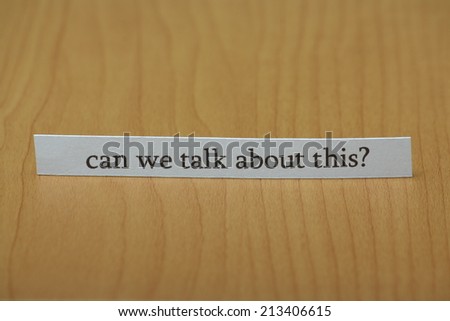 The question can we talk about this typed on a strip of paper left standing on a wooden desktop