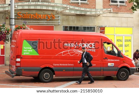 Reading, England - August 28th, 2014: A man walks past a Parcelforce van parked in front of a Sainsbury\'s supermarket. The UK based Parcelforce delivers to 240 countries and territories worldwide