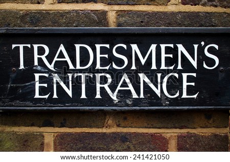 Tradesman\'s Entrance sign on the exterior brick wall of a building. Once common in British society and ridiculed as part of the class system, the entrance was usually around the back of the premises