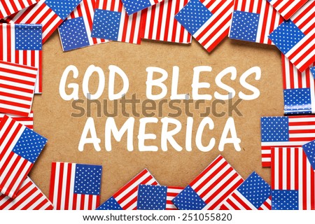 The phrase God Bless America in white text on a brown card background with a border of miniature flags of the United States of America
