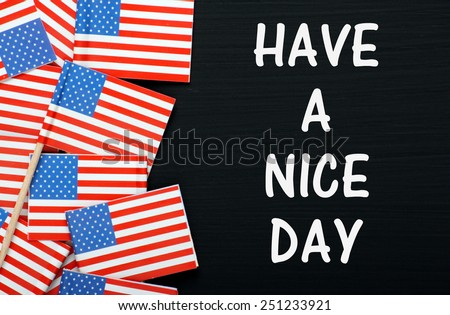 The phrase Have A Nice Day in white text on a blackboard next to miniature flags of the United States of America