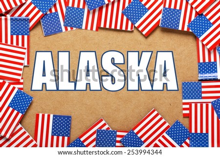 Miniature flags of the United States of America form a border on brown card around the name of the state of Alaska