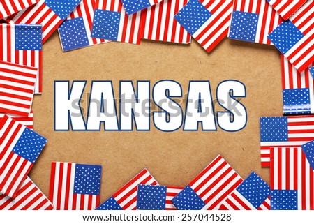 Miniature flags of the United States of America form a border on brown card around the name of the state of Kansas