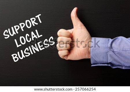 Male hand wearing a business shirt giving the Thumbs Up gesture to the phrase Support Local Business written on a blackboard