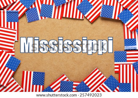 Miniature flags of the United States of America form a border on brown card around the name of the state of Mississippi