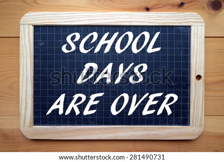 The phrase School Days Are Over in white ext on a slate blackboard placed flat on a wooden surface