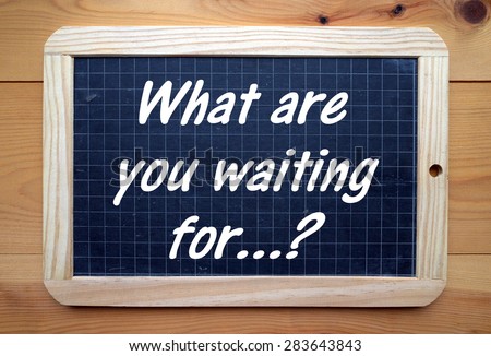The question What Are You Waiting For? in white text on a slate blackboard placed on a flat wooden surface
