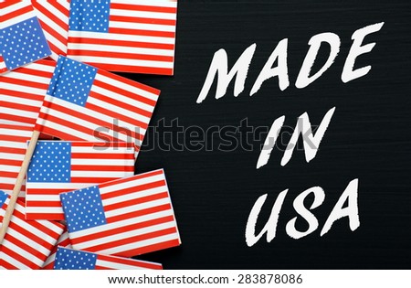 The phrase Made In USA in white text on a blackboard next to miniature stars and stripes flags
