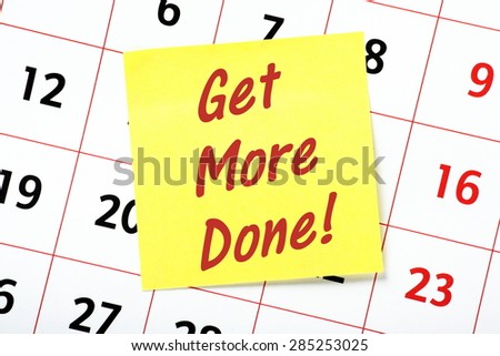 The phase Get More Done! in red text on a yellow sticky note attached to a wall calendar