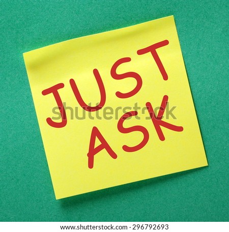 The phrase Just Ask in red text on a yellow sticky note posted on a green notice board as a reminder