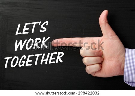 Male hand wearing a business shirt pointing at the phrase Let\'s Work Together in white text on a blackboard
