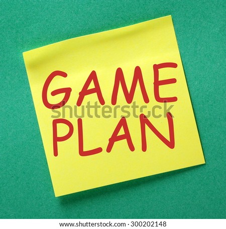 The phrase Game Plan in red text on a yellow sticky note posted on a green notice board as a reminder