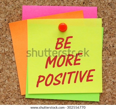 The phrase Be More Positive in red text on a yellow sticky note pinned to a cork notice board as a reminder of your new resolution