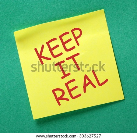 The phrase Keep It Real in red text on a yellow sticky note posted on a green notice board as a reminder