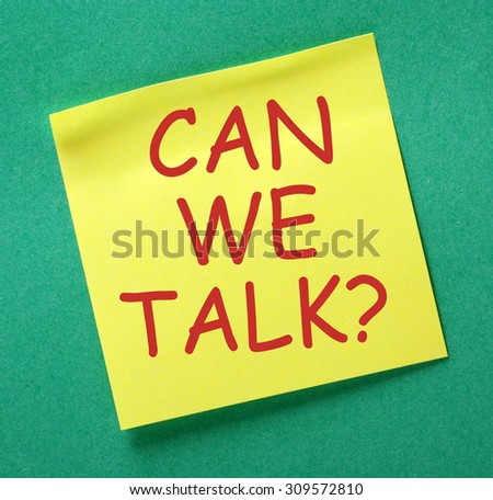 The phrase Can We Talk? in red text on a yellow sticky note posted on a green notice board as a reminder that discussion and dialog works