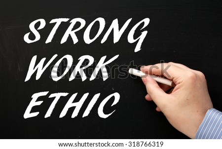Hand writing the phrase Strong Work Ethic in white text on a blackboard as a reminder of the characteristics required for success