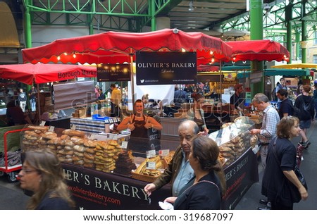 London, England - August 20, 2015: People walk by whilst someone is being served by staff at a bakery stall in Borough Market, London. A market has traded in Southwark, London for more than 250 years
