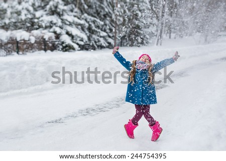 Cute six year old girl dressed in a blue coat and a pink hat and boots, hamming and playing in the winter forest