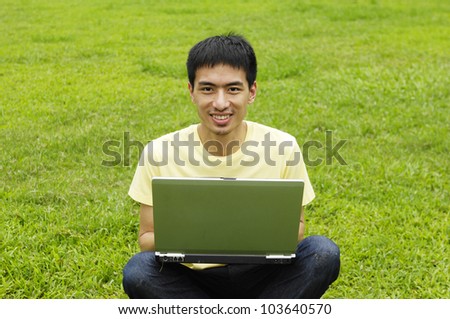 Male university student sitting on the grass working on laptop at campus