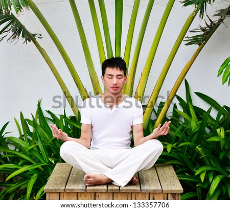 A young man doing yoga in Nature sitting wooden chair