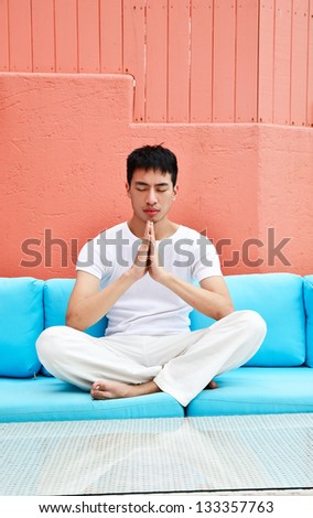young man doing yoga meditation, sitting in living room.