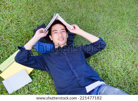 Asian university student relaxing on grass with a tablet ,book at university campus
