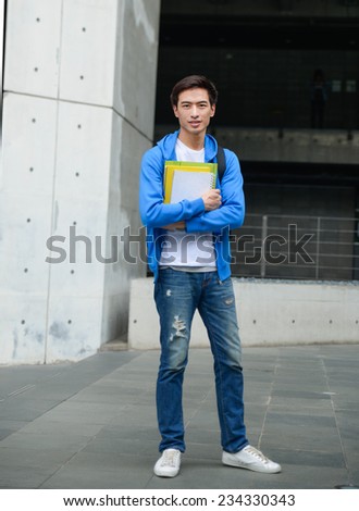 Full body portrait of college student standing holding book at his university