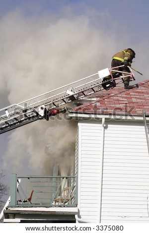 A fireman climbing onto the roof of a house on fire