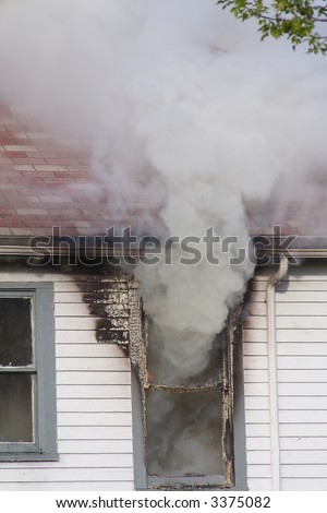 Smoke pouring out of the second story window in a house that is on fire