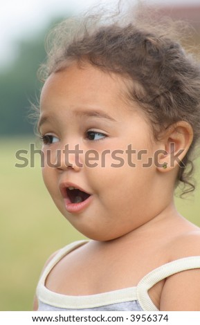A close-up of a surprised toddler girl standing outside