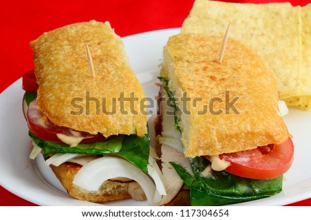 Turkey, Ham and Roast Beef cold cuts on Ciabatta bread with tomatoes, onions, lettuce and Chipotle Mayonnaise with tortilla chips against red background.