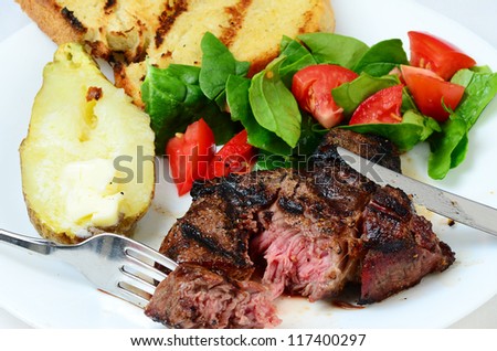 Bite cut out of juicy rib eye steak grilled to perfection and served with baked potato and Texas Toast.