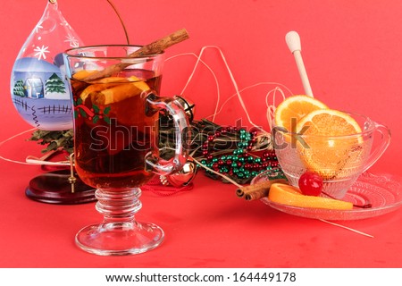 Gluhwein or Mulled Wine in clear glass drink mug with holiday decoration.  Christmas scene with beads, bells and scented herbs on red background.