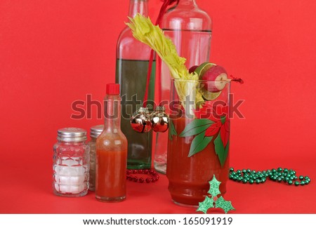 Bloody Mary Cocktail garnished with radish, lime and celery stick on red background with Christmas ornaments and vintage liquor bottles.
