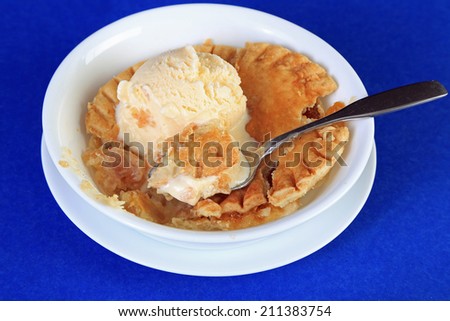 Scoop of vanilla ice cream on individual baked peach pie in white bowl on blue background.