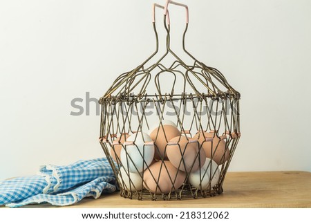 Vintage wire egg basket filled with fresh farm eggs on kitchen counter with plain background.