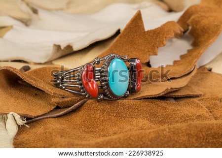 Native American Bracelet of Turquoise and Coral set in Sterling Silver against scrap pieces of suede and buckskin leather.