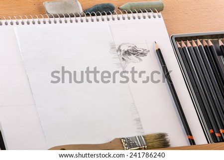 Sketch pad with partially completed image and art equipment on wooden easel.  Shading a dog drawing.