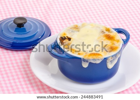 Melted cheese baked golden brown  pouring over edge of blue bowl  of French Onion Soup.  Strong light from behind blue bowl sitting on pink gingham tablecloth.