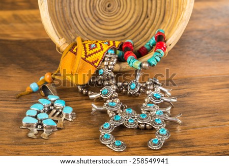 Beautiful turquoise and silver symbolic Native American jewelry spilling from vintage wicker basket onto rustic wooden floor.