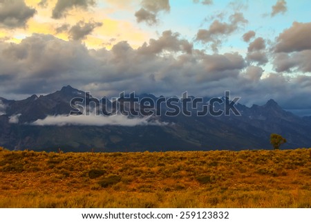 Low hanging clouds shroud Teton Mountains at sunset after summer storm dropped snow and rain in upper levels of Grand Teton National Park, Wyoming.