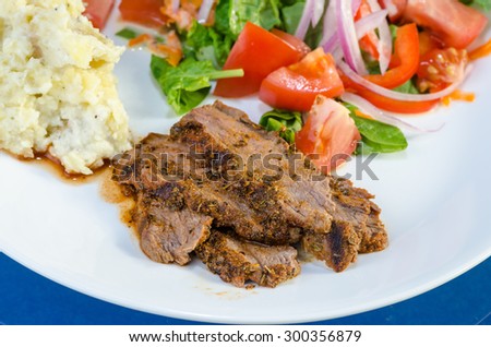 Closeup of flank steak cooked in jerk sauce and served with mashed potatoes and salad.