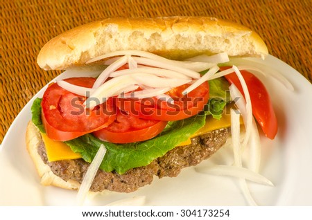 Grilled hamburger with cheese stretched to fit on hot dog bun.  Onions, lettuce and tomatoes.