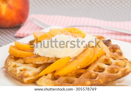 Golden brown waffle topped with juicy sliced peaches and whipped cream.