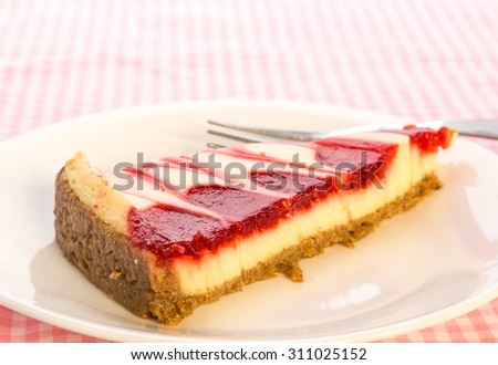 Bright back lighting on slice of strawberry swirl cheesecake on pink gingham tablecloth.