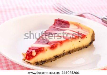Bright back lighting on slice of strawberry swirl cheesecake on pink gingham tablecloth.  Closeup with selective focus and shallow dof.