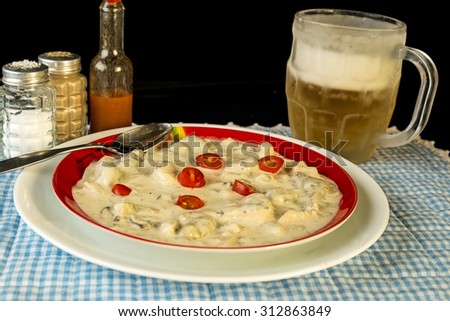 Large plate of crab chowder filled with oyster and shrimp and garnished with sliced tomato.  Served with cold beer in frosted mug.